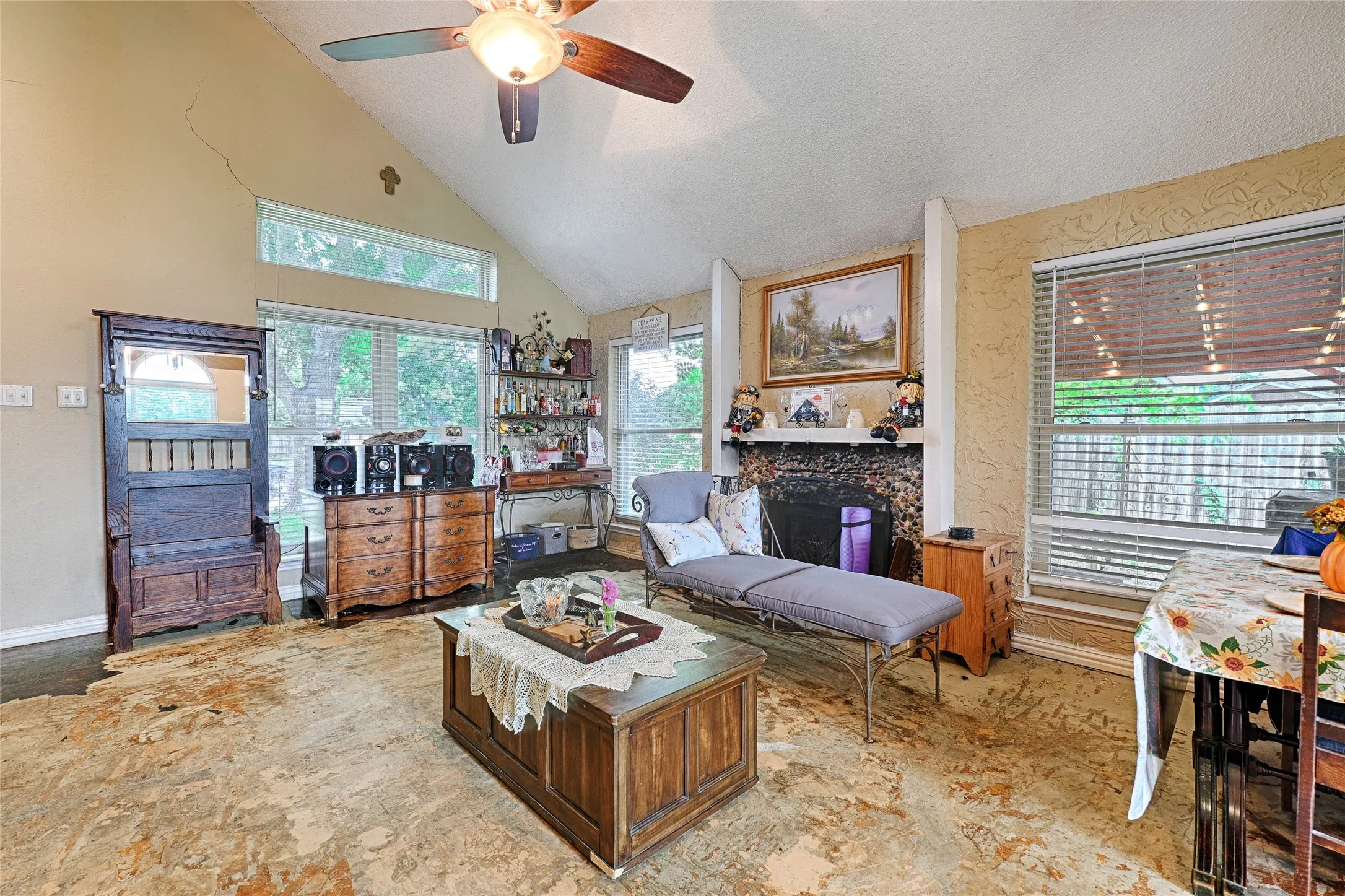 Vaulted ceiling with a ceiling fan, full-height windows, additional transom windows, a stone-faced fireplace, and an adjacent dining area