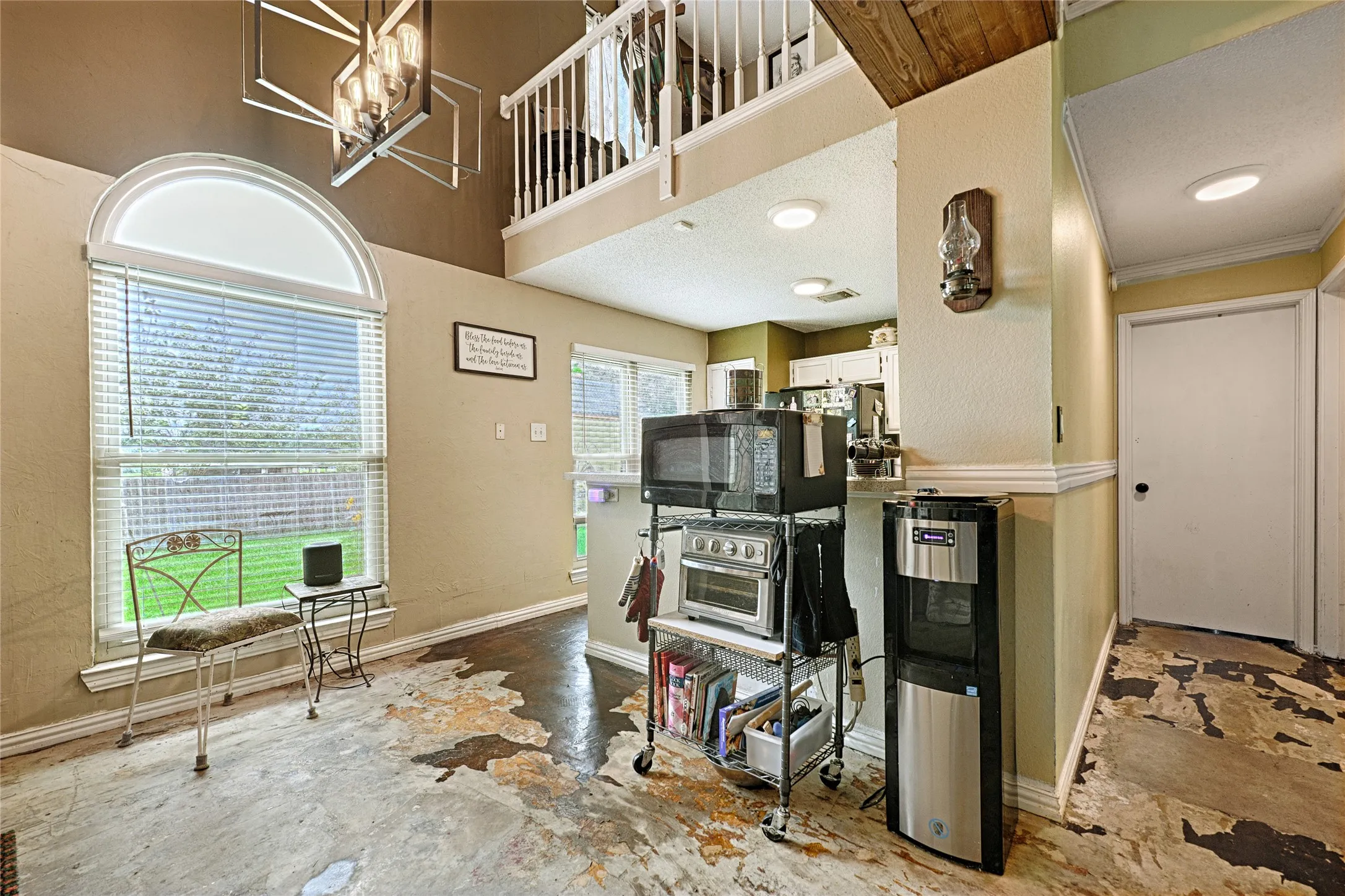 Two-story living area featuring a large arched window, a modern geometric chandelier, and an upper-level balcony with white railings