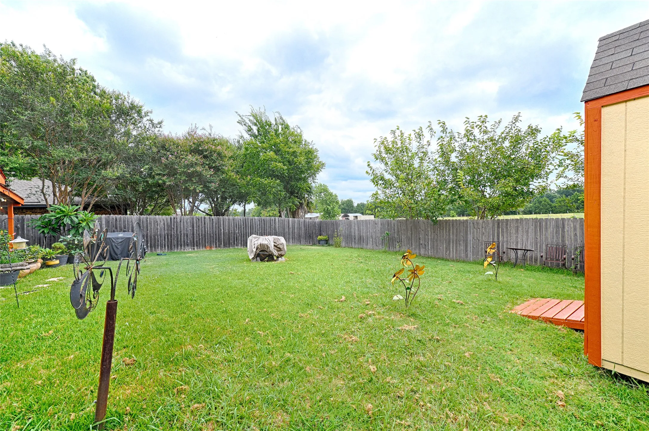 Expansive backyard featuring a lush lawn, privacy fencing, mature trees, and a storage shed with a shingled roof
