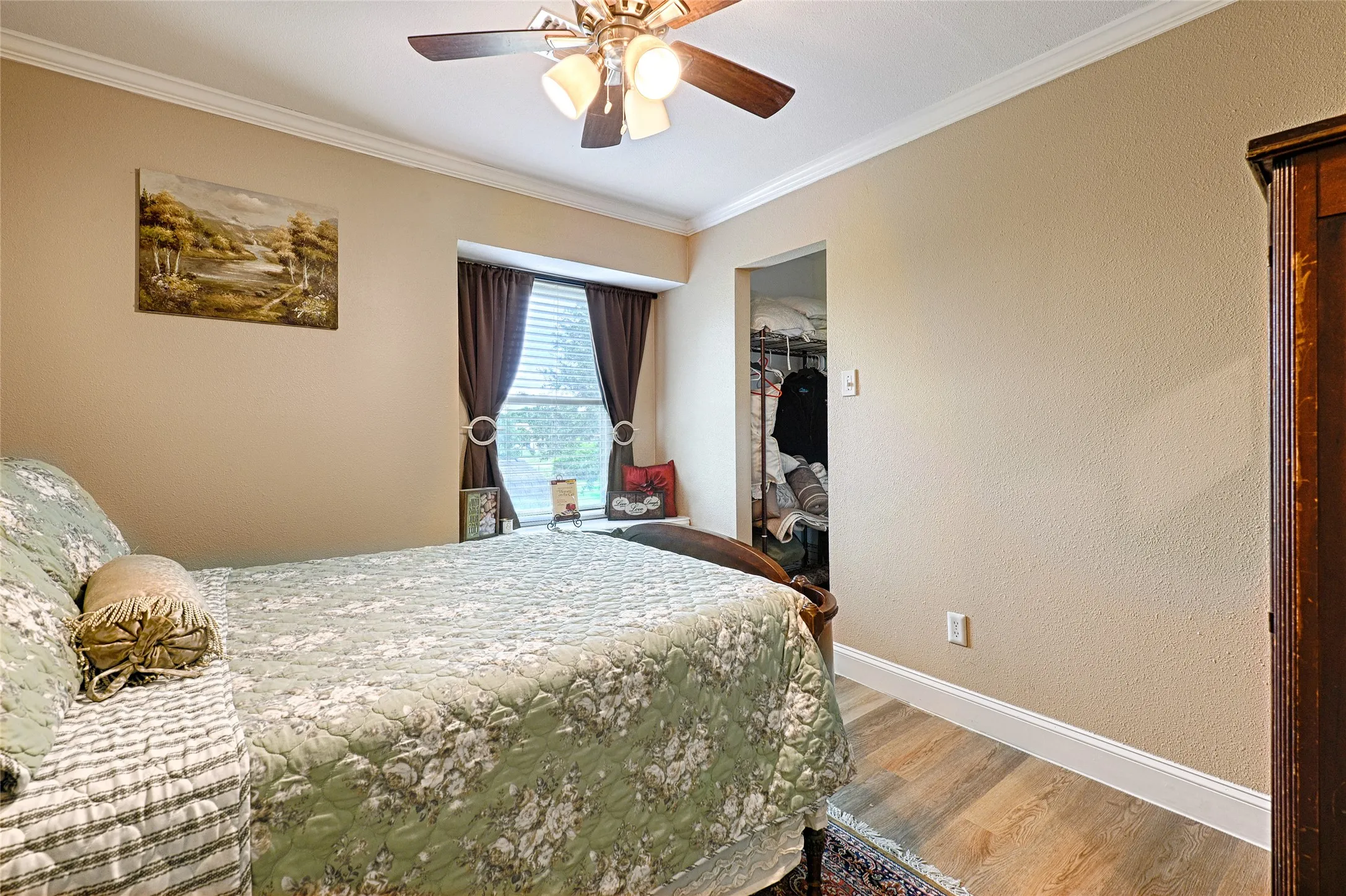 Bedroom featuring a window with blinds and drapes, a ceiling fan with integrated lighting, crown molding, and wood-finish flooring