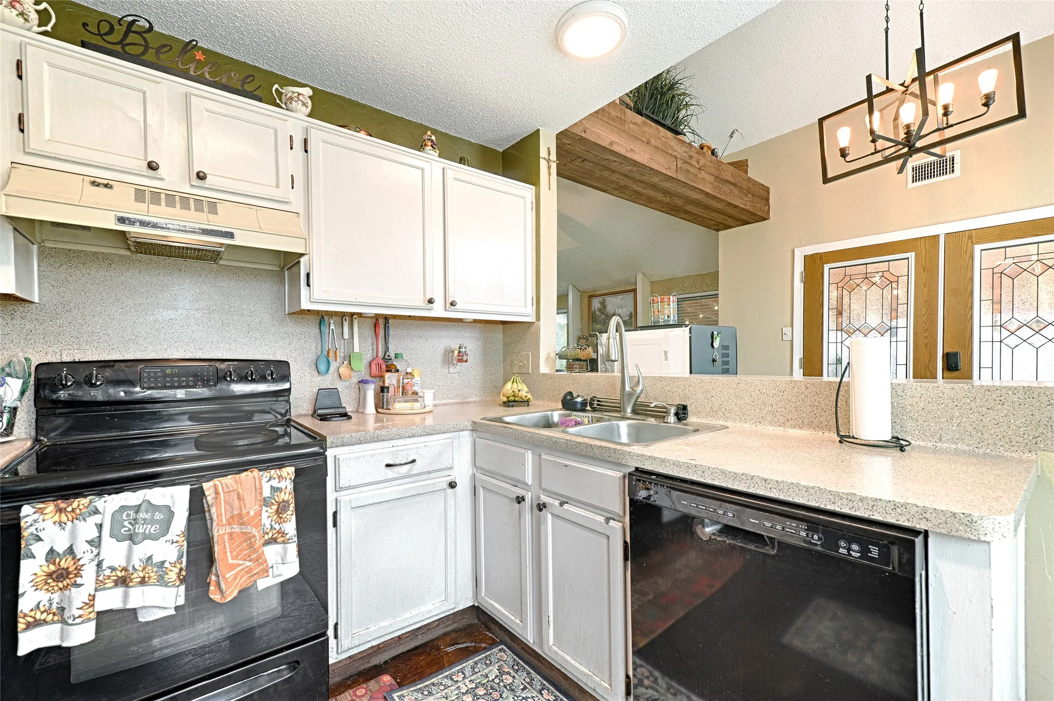 Kitchen featuring white cabinetry, a black electric range, a black dishwasher, a double basin stainless steel sink, and light speckled countertops