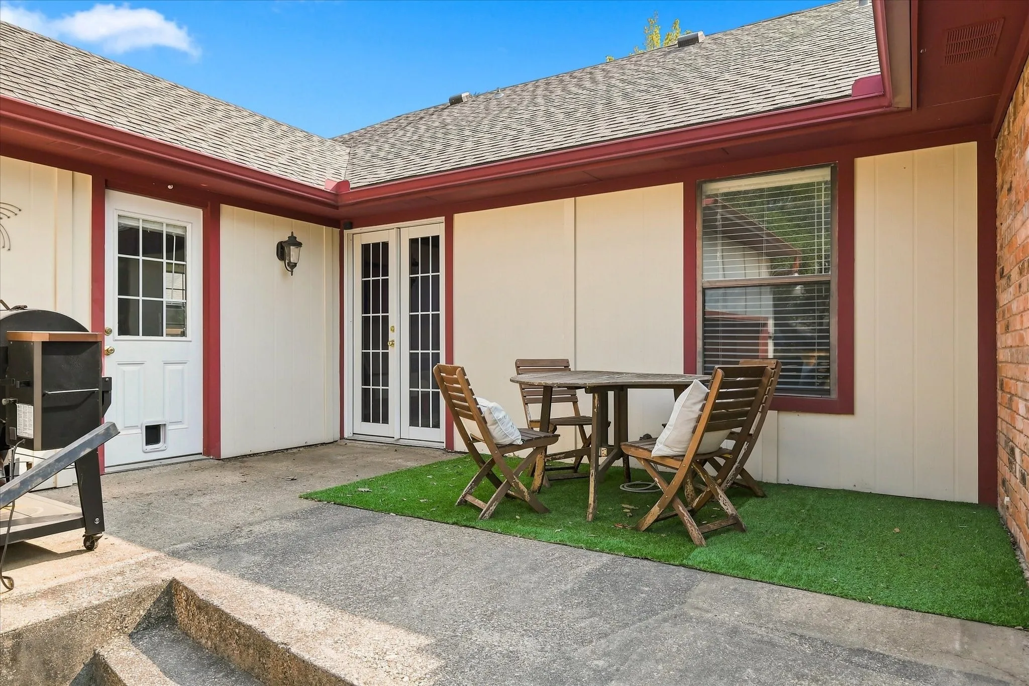 Covered patio retreat featuring a composite decking surface, complemented by a manicured synthetic lawn, outdoor seating area, and direct access to the home via French doors