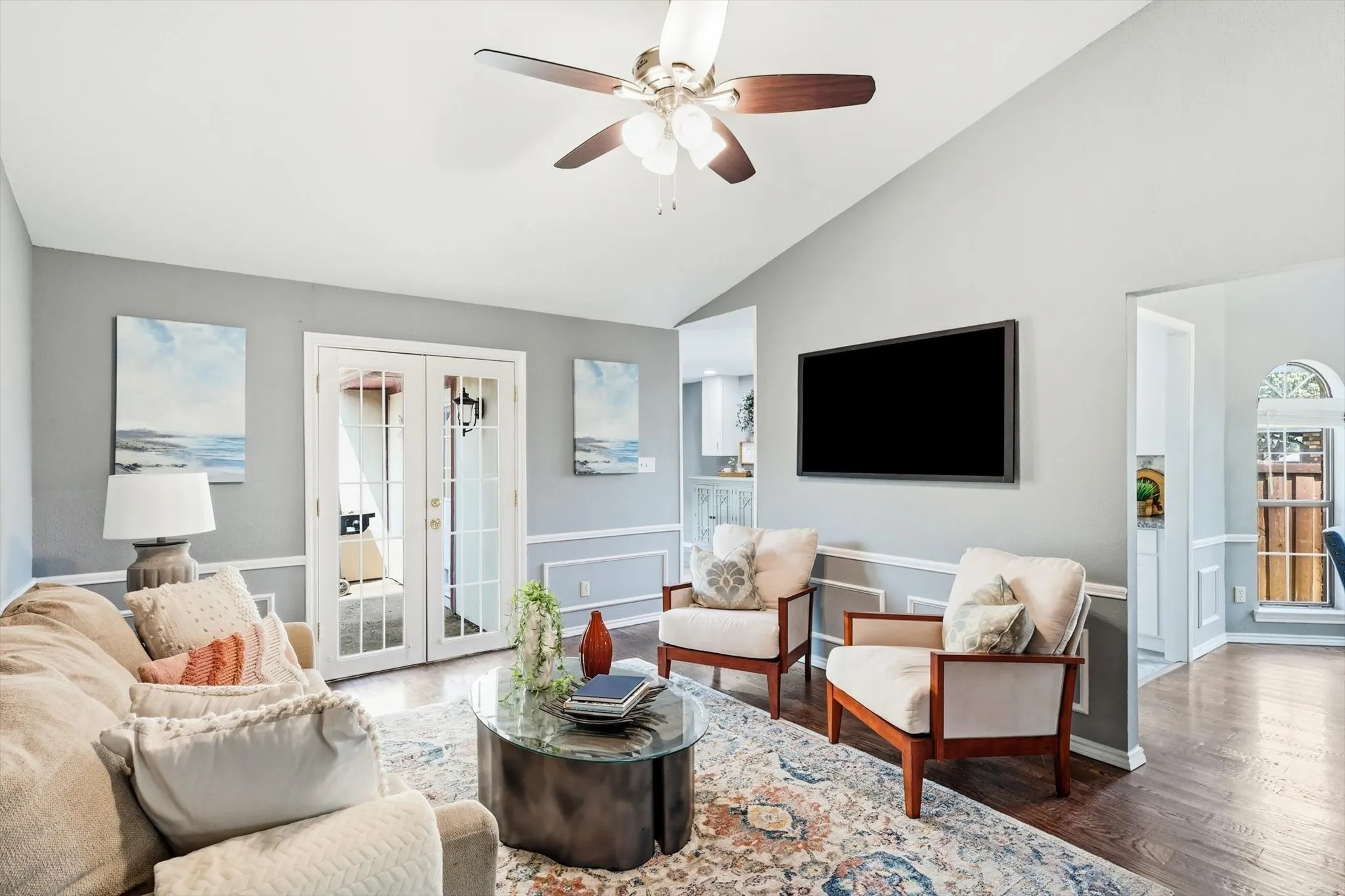 Vaulted ceiling with a ceiling fan, French doors, hardwood flooring, and decorative wainscoting