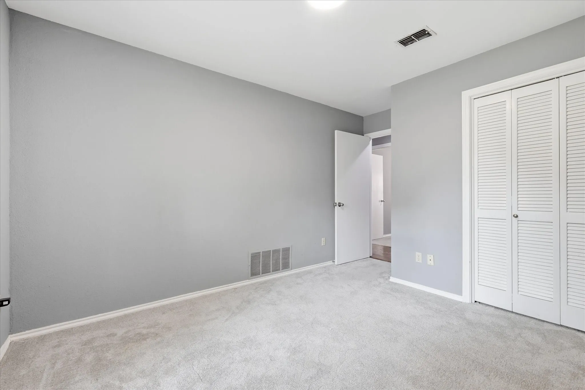 Wall-to-wall carpeting with light gray walls, featuring a louvered bi-fold closet door and white trim