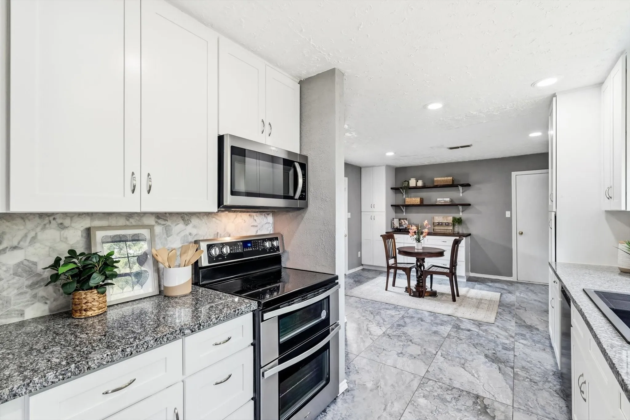 Modern kitchen featuring white cabinetry with brushed nickel hardware, granite countertops, and stainless steel appliances including a double wall oven and microwave