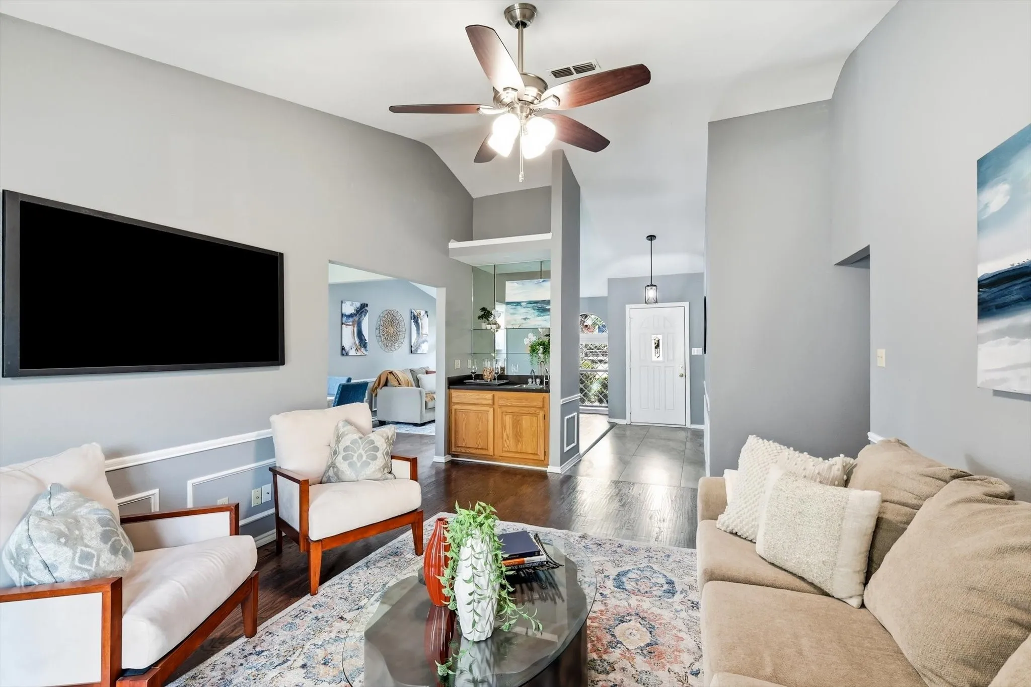 Bright and open living space anchored by a wall-mounted flat-screen television, ceiling fan with integrated lighting, and polished concrete flooring throughout