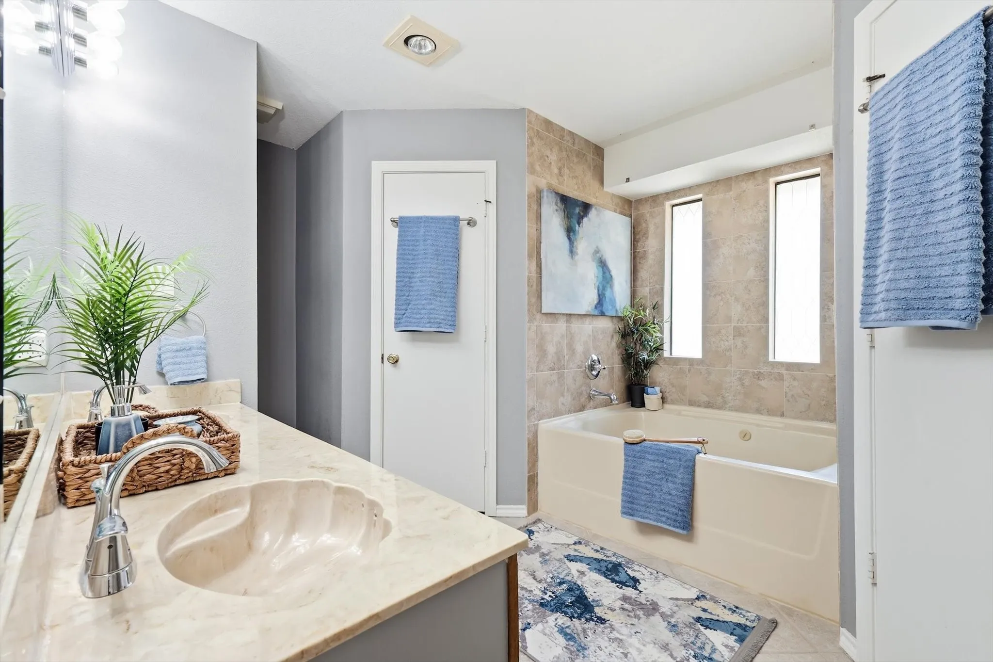 Modern primary bathroom featuring a light-finish vanity with an undermount sink and quartz countertop, chrome faucet, large framed mirror, and neutral tile surround