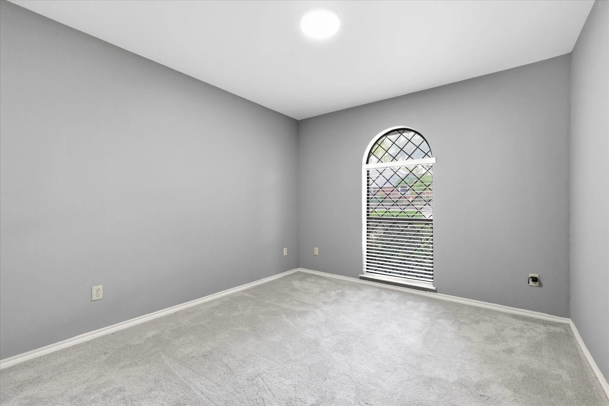 Spacious bedroom with neutral gray walls, recessed ceiling lighting, and arched transom window with security bars providing natural light