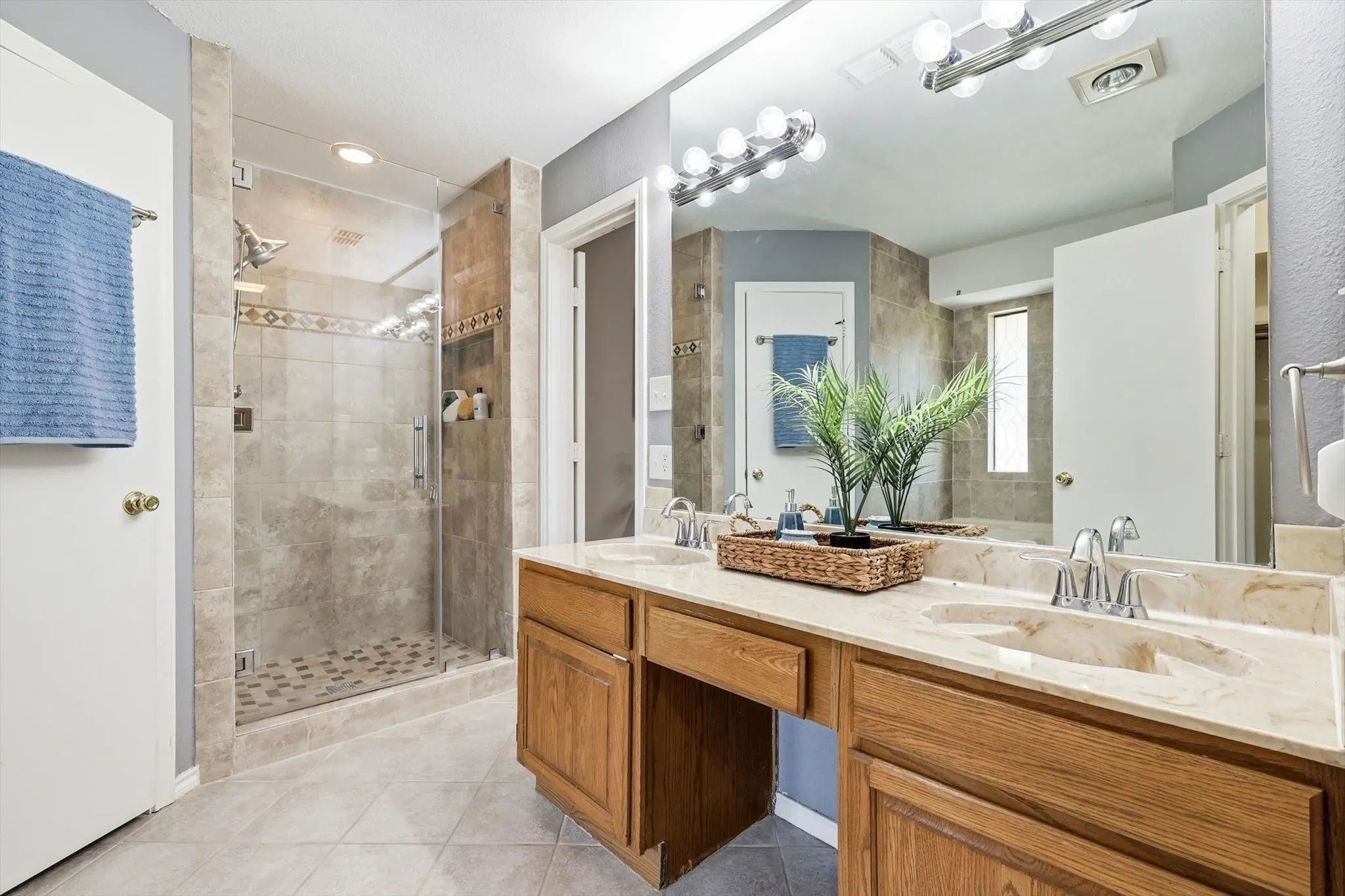 Dual vanity with stone countertop and integrated sinks, wood-finish cabinetry, and an expansive mirror