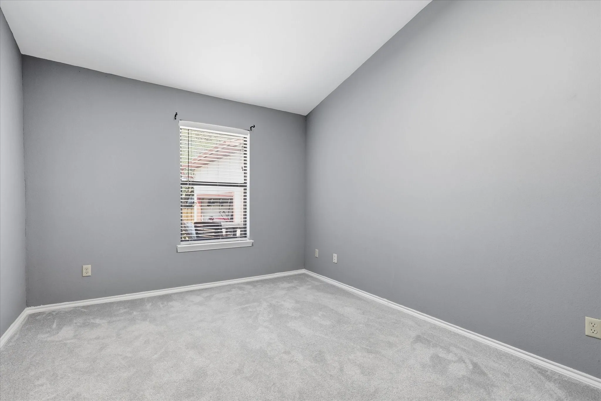 Bright bedroom featuring neutral gray walls, carpeted flooring, large double-hung window with blinds, and recessed lighting throughout the ceiling