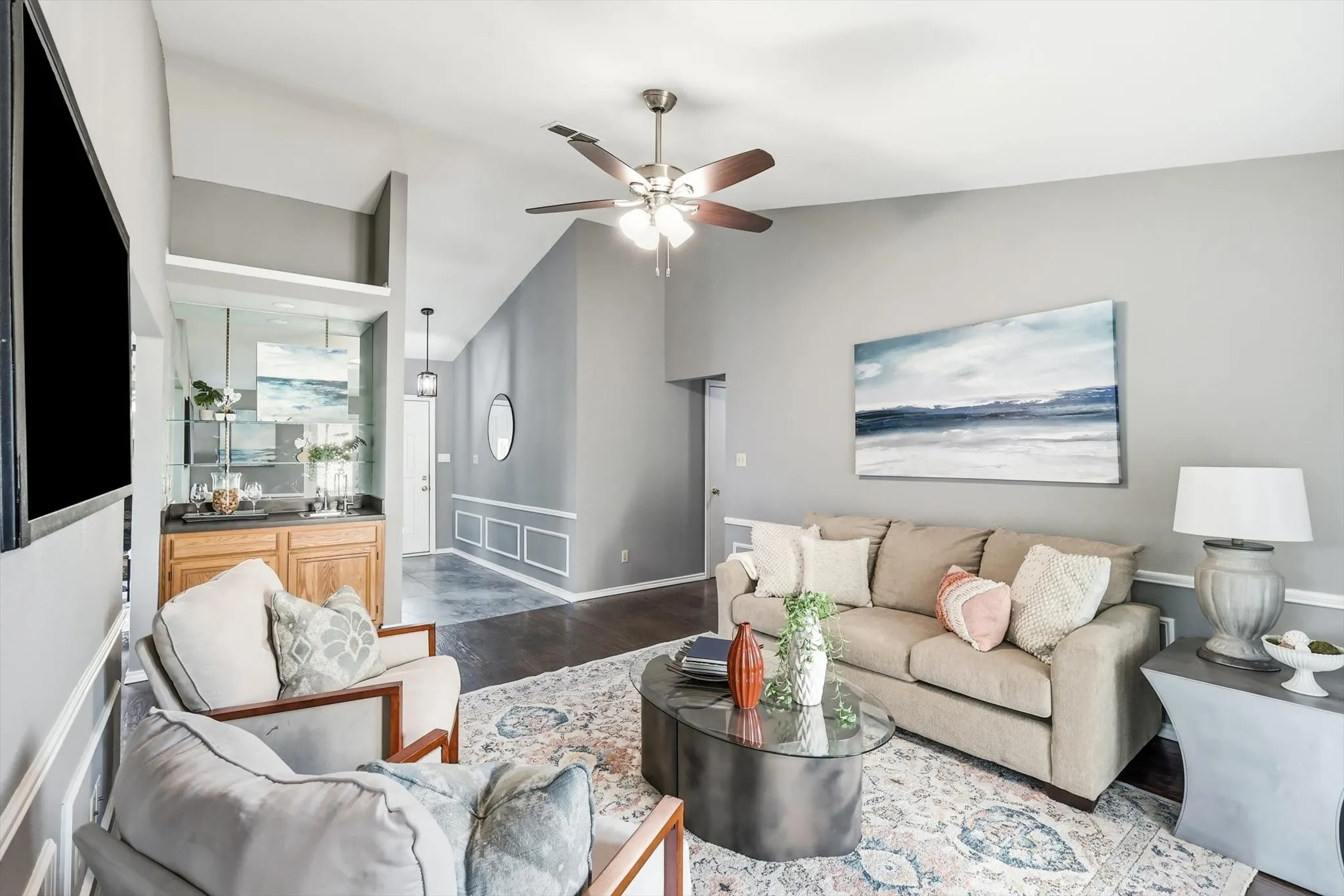 Open-concept living area featuring neutral gray walls, wood-finish flooring, and a ceiling fan with integrated lighting
