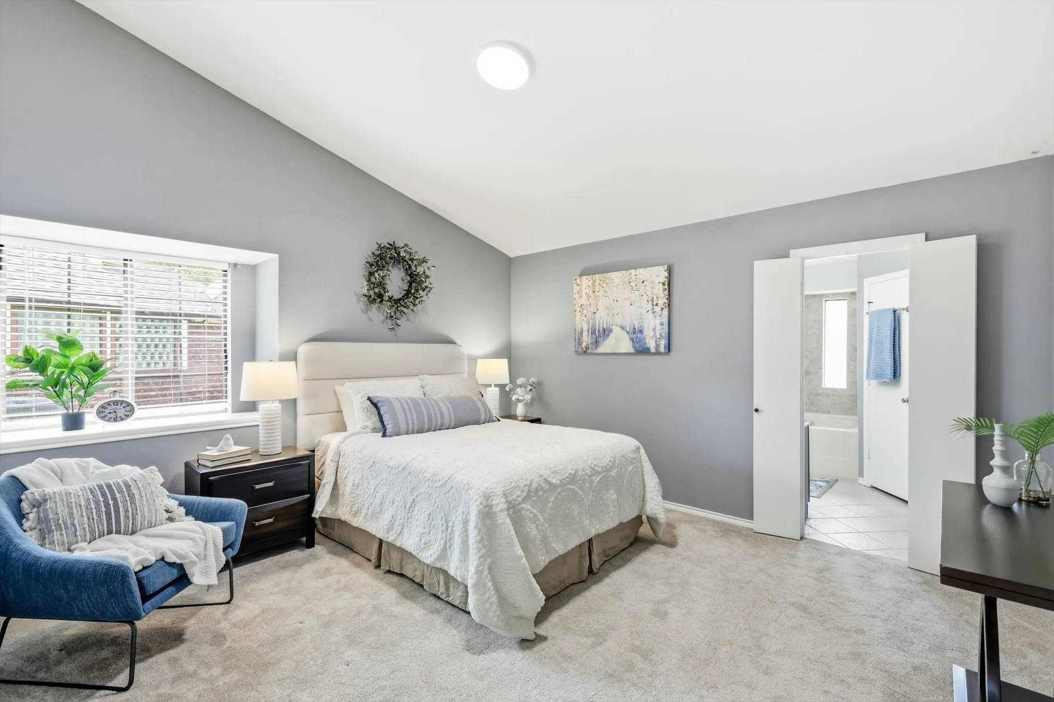 Serene primary bedroom suite featuring soft gray walls, a neutral upholstered headboard, recessed ceiling lighting, and direct access to an ensuite bathroom