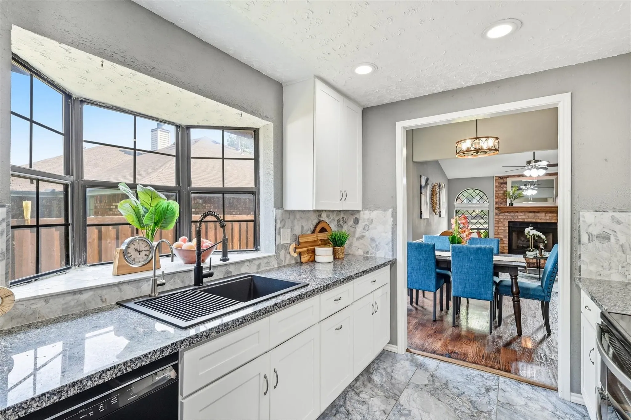 Modern kitchen featuring white cabinetry, granite countertops, a black double basin sink with a black faucet, and a large bay window