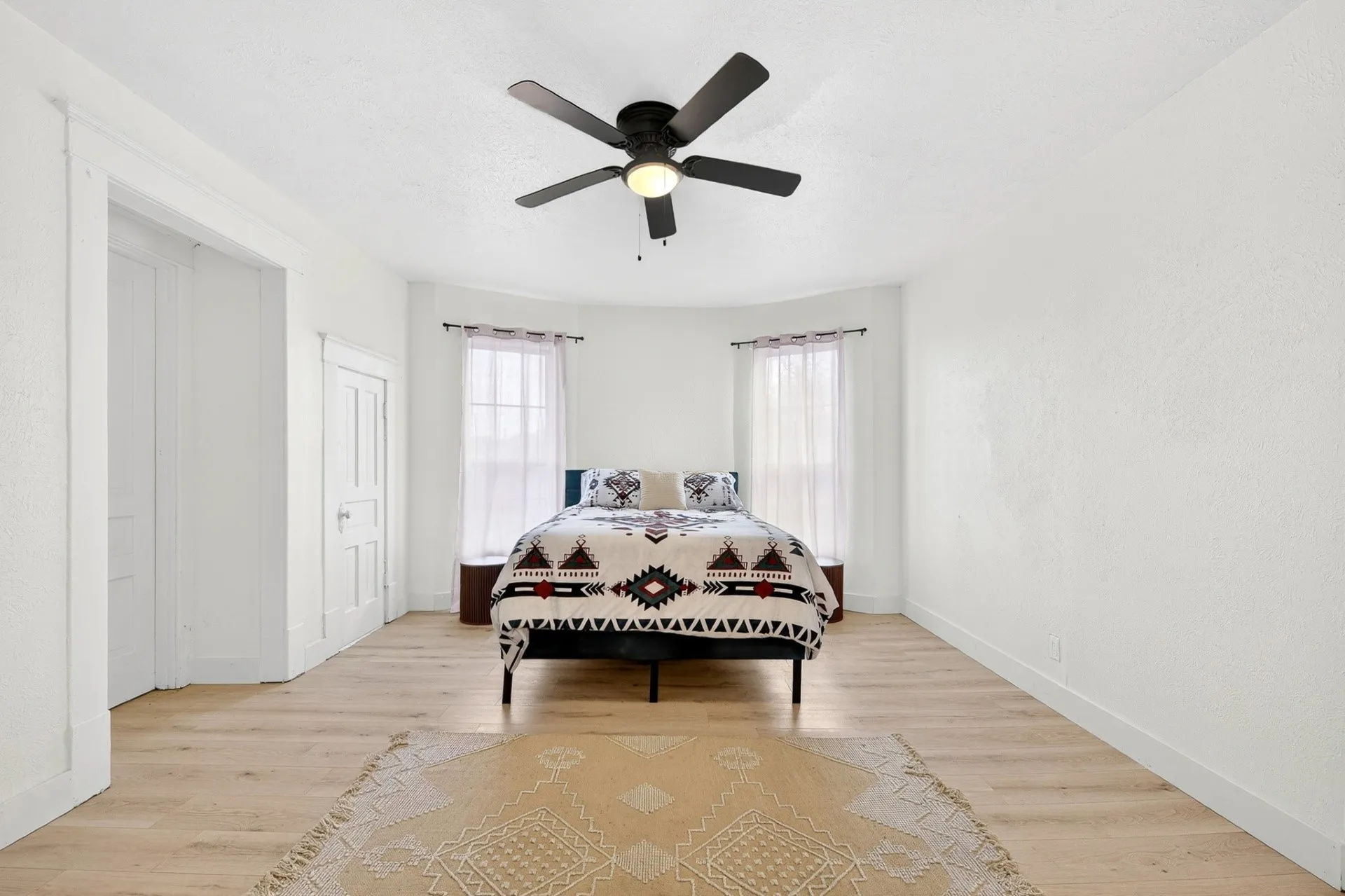 Spacious room featuring wood-finish flooring, a contemporary ceiling fan, and two large windows