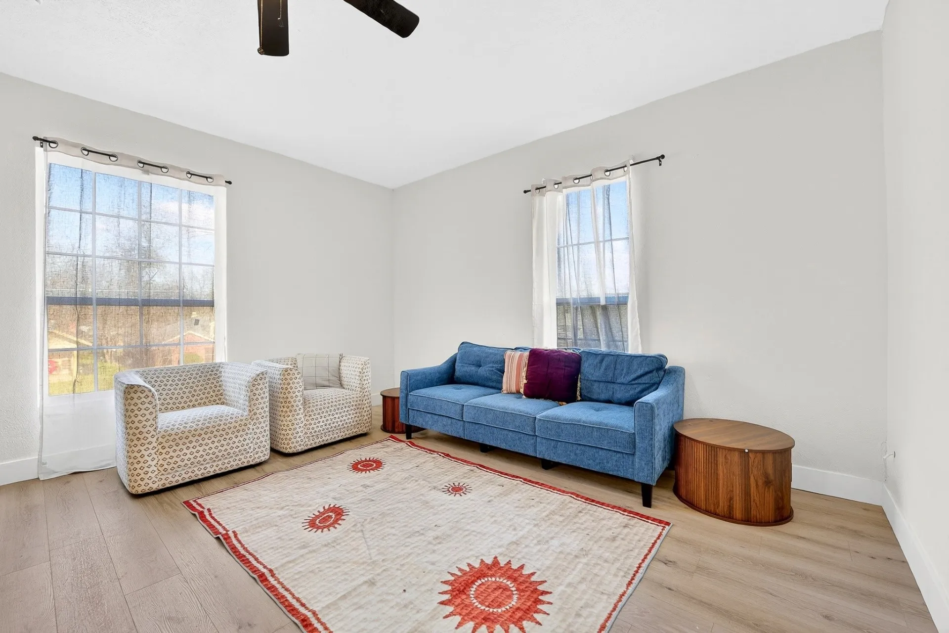 Bright room featuring two large windows, light wood-finish flooring, white walls, and a ceiling fan