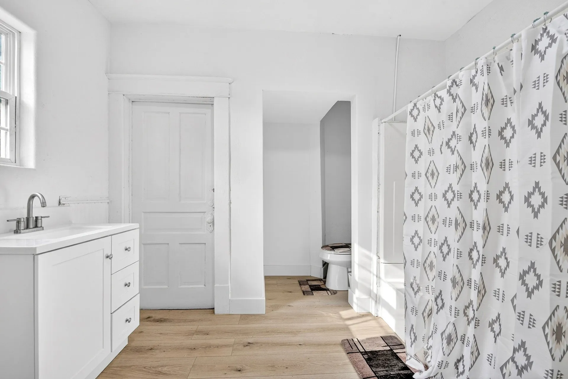 Bathroom with light wood-finish flooring, white vanity with nickel hardware, and a window providing natural light