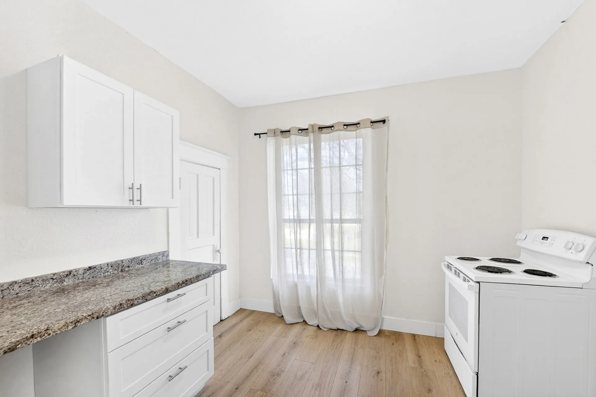 Kitchen space featuring white cabinetry with silver hardware, speckled countertops, wood-finish flooring, and a white electric range