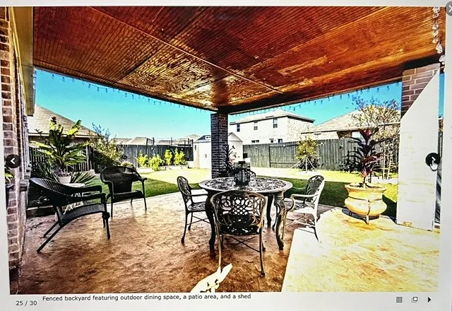 Covered outdoor patio with a stained wood-finish ceiling, string lighting, brick columns, and a stamped concrete floor