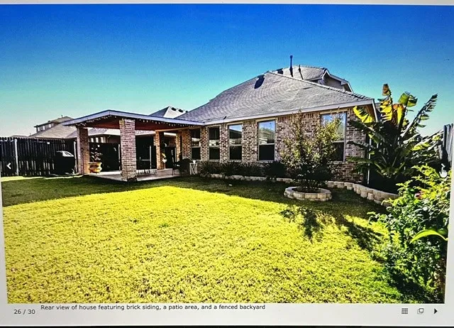 Spacious backyard featuring a covered patio, brick siding, a manicured lawn, and perimeter fencing