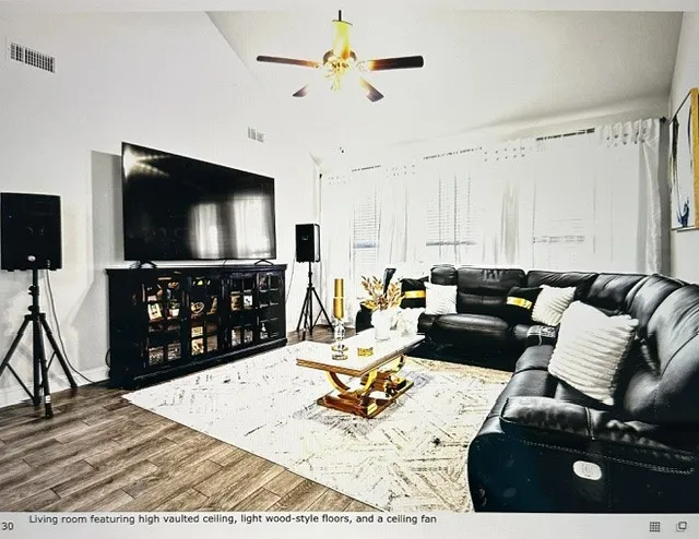 Living room featuring high vaulted ceiling, light wood-style floors, and a ceiling fan