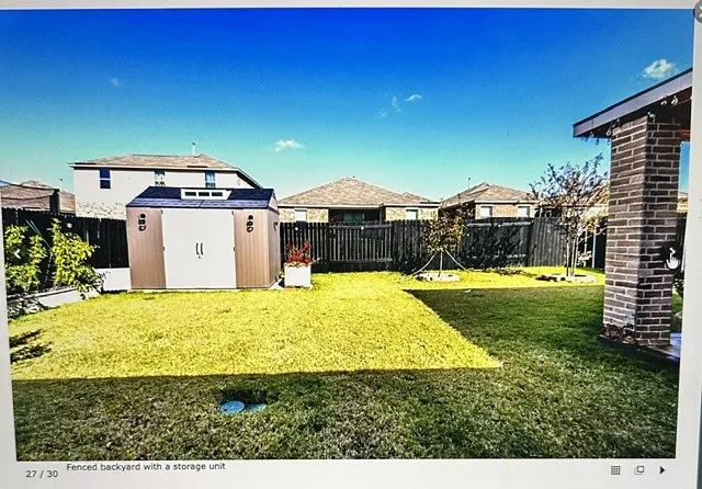 Expansive green lawn with a brown and white storage shed, surrounded by dark wood privacy fencing