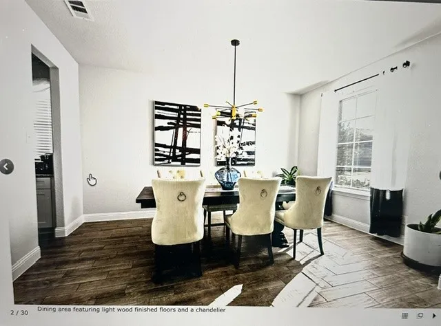 Dining area featuring wood-finish flooring, a modern chandelier, and ample natural light from a large window