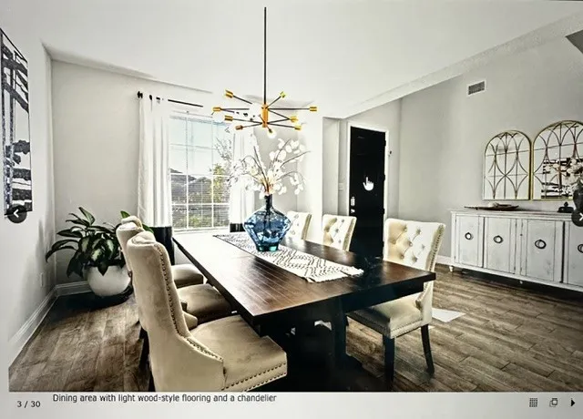 Dining area featuring wood-finish flooring, a contemporary chandelier, a window with white curtains, and light-toned walls