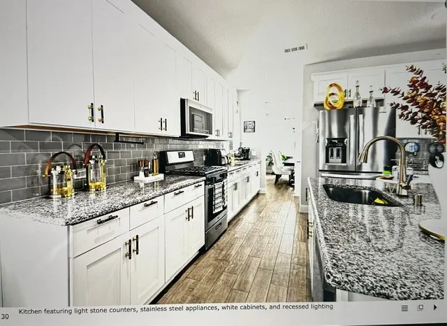 Kitchen featuring white cabinetry, light stone countertops, stainless steel appliances, grey subway tile backsplash, and wood-finish flooring