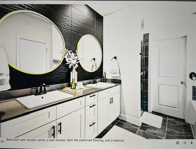 Modern bathroom featuring a double vanity with white cabinetry and dark countertops, accented by two gold-framed circular mirrors