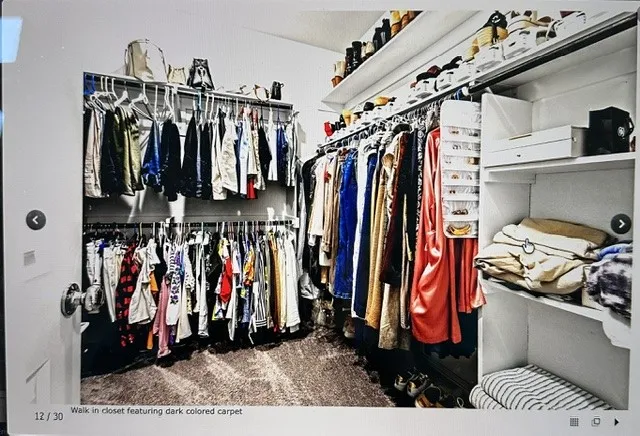 Walk-in closet featuring built-in shelving, hanging rods, and dark carpeting