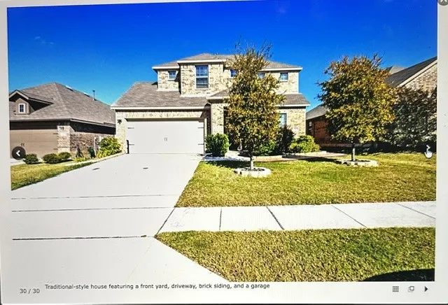 Traditional-style house featuring a front yard, driveway, brick siding, and a garage