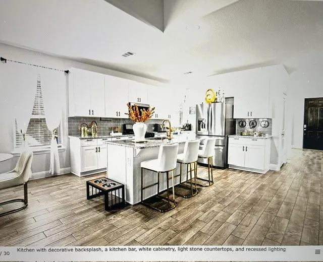 Spacious kitchen featuring wood-finish flooring, white cabinetry, light stone countertops, a decorative backsplash, and recessed lighting