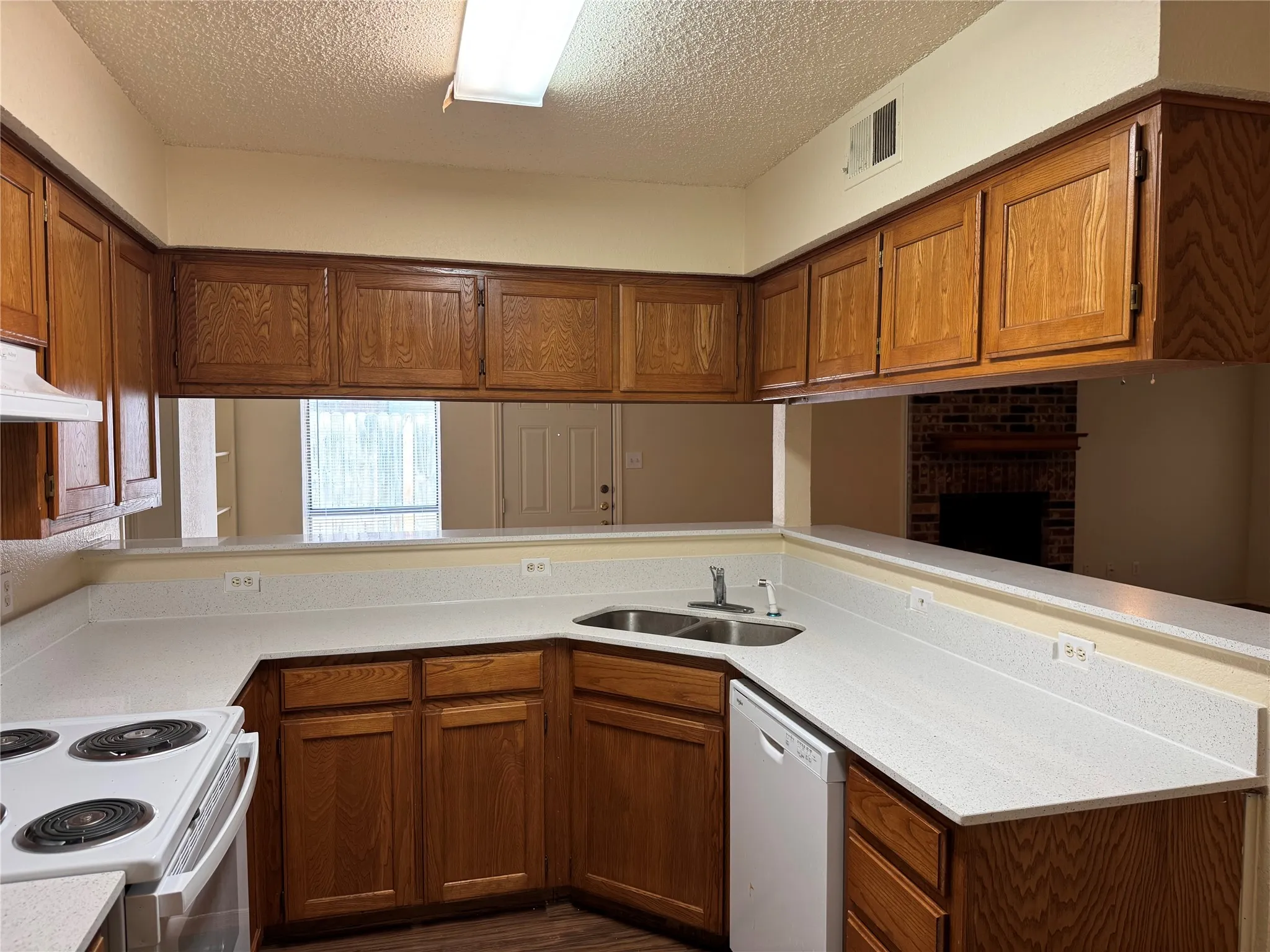 Kitchen featuring wood-finish cabinetry, light-toned countertops, a built-in double basin sink, and a white dishwasher