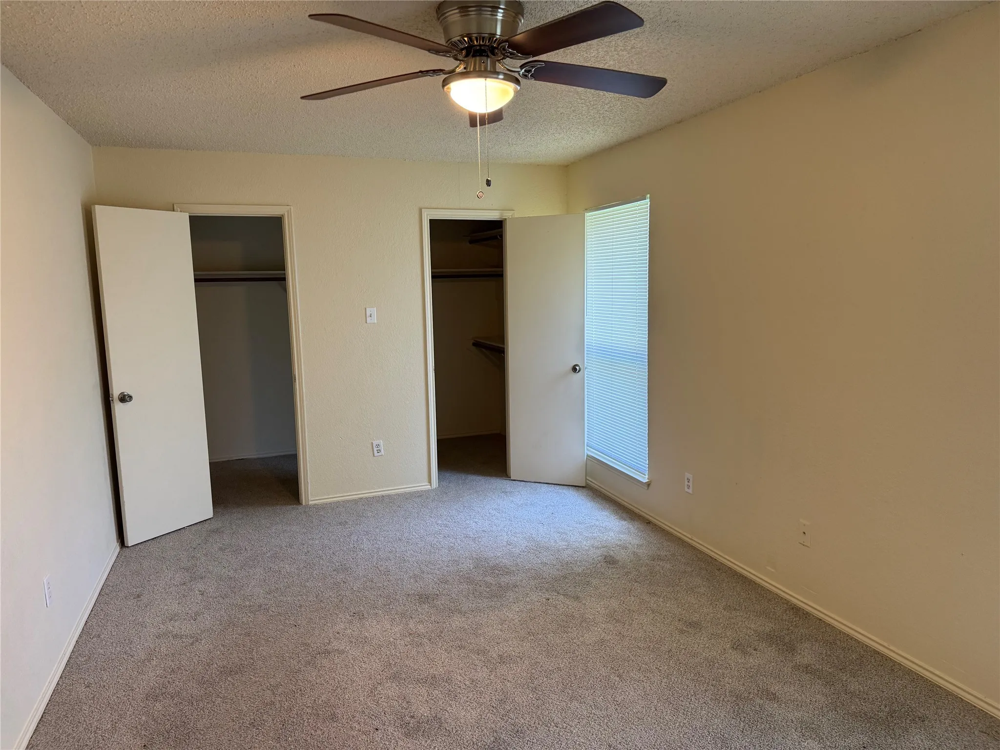 Carpeted room featuring a ceiling fan with integrated lighting, a window with horizontal blinds, and two closet entrances
