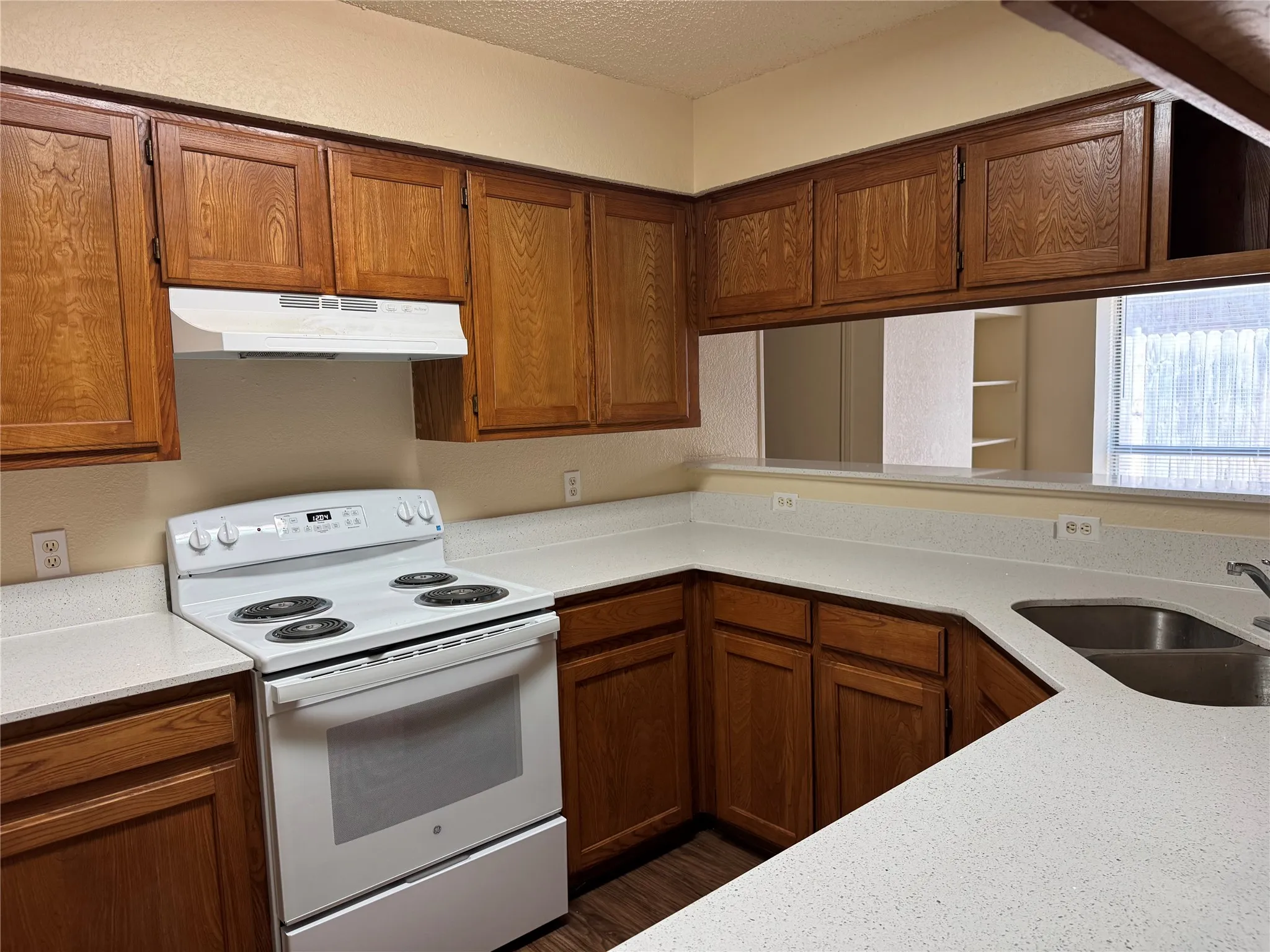 Functional kitchen featuring extensive wood cabinetry, white countertops, a built-in range with an overhead vent, and a stainless steel double-basin sink