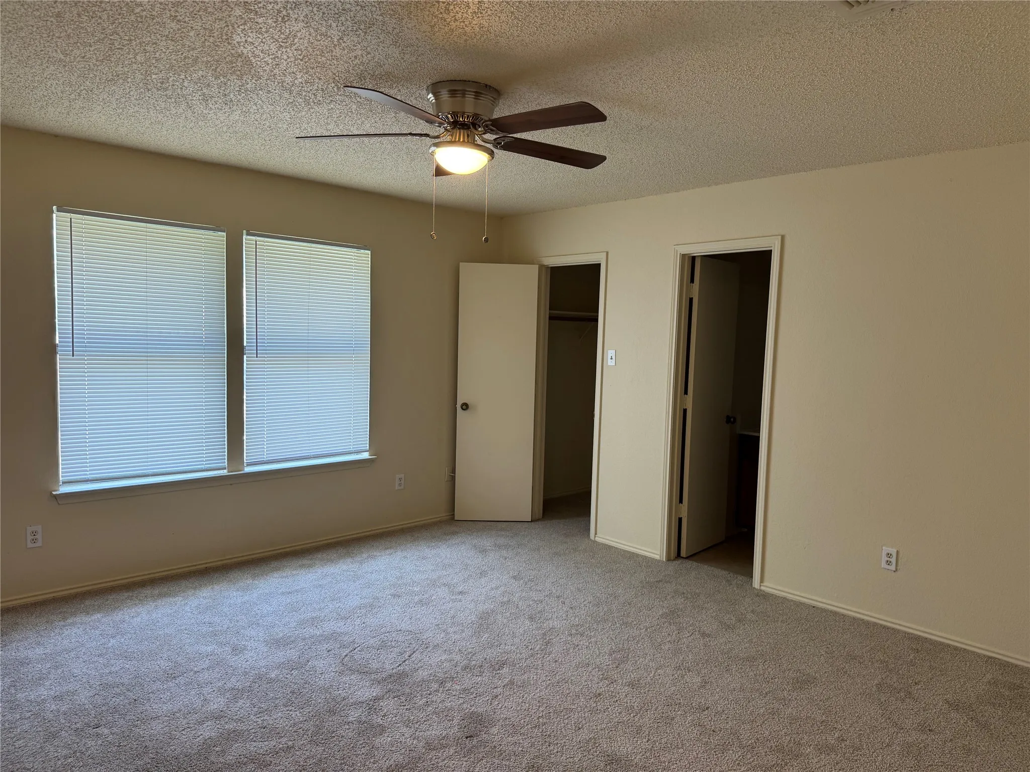 Carpeted room featuring dual windows with blinds, a ceiling fan with integrated lighting, and two interior doorways