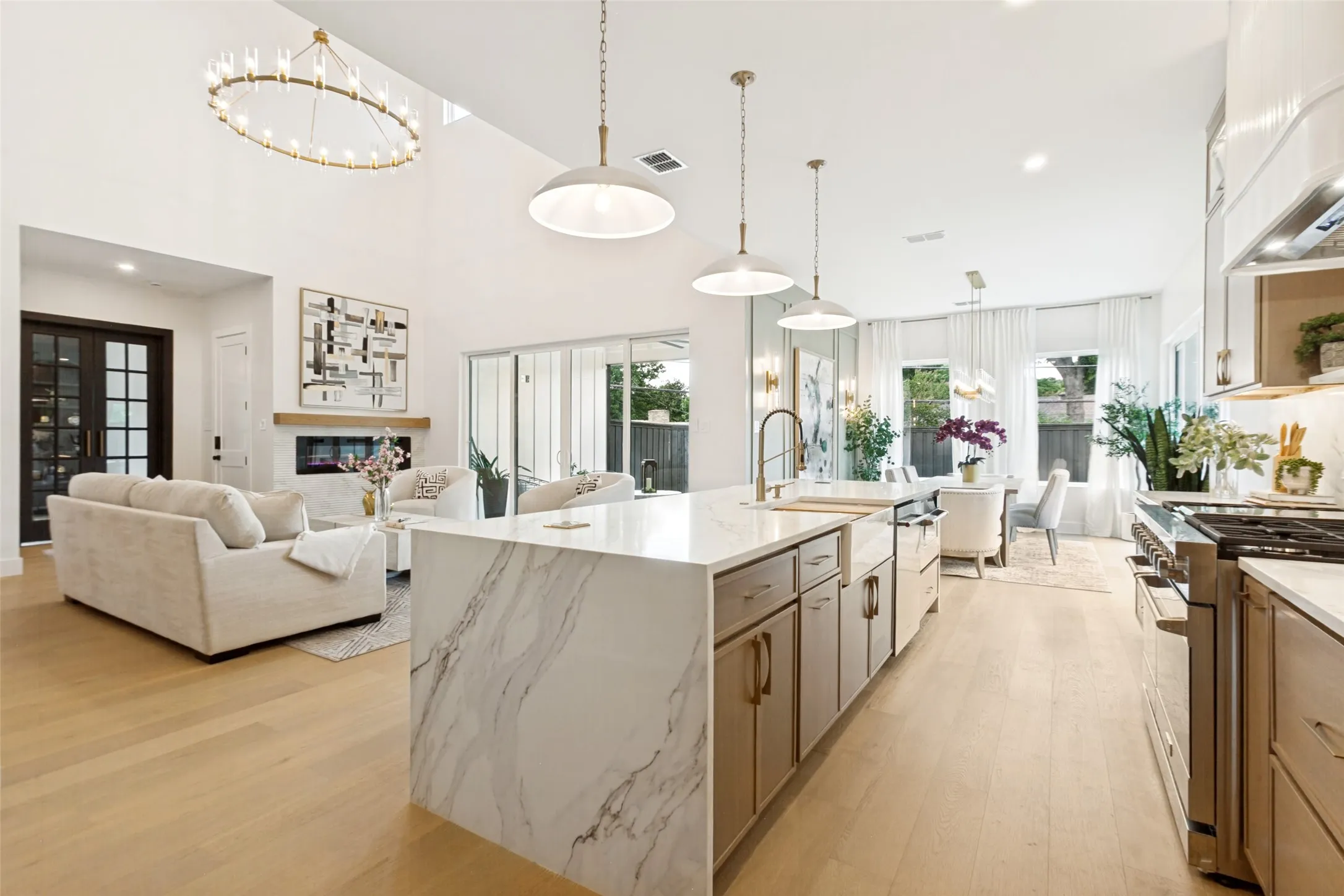 Expansive open-concept living area featuring high ceilings, oak wood flooring, a contemporary fireplace,designer light fixtures and an oversized kitchen island with a quartz waterfall countertop.