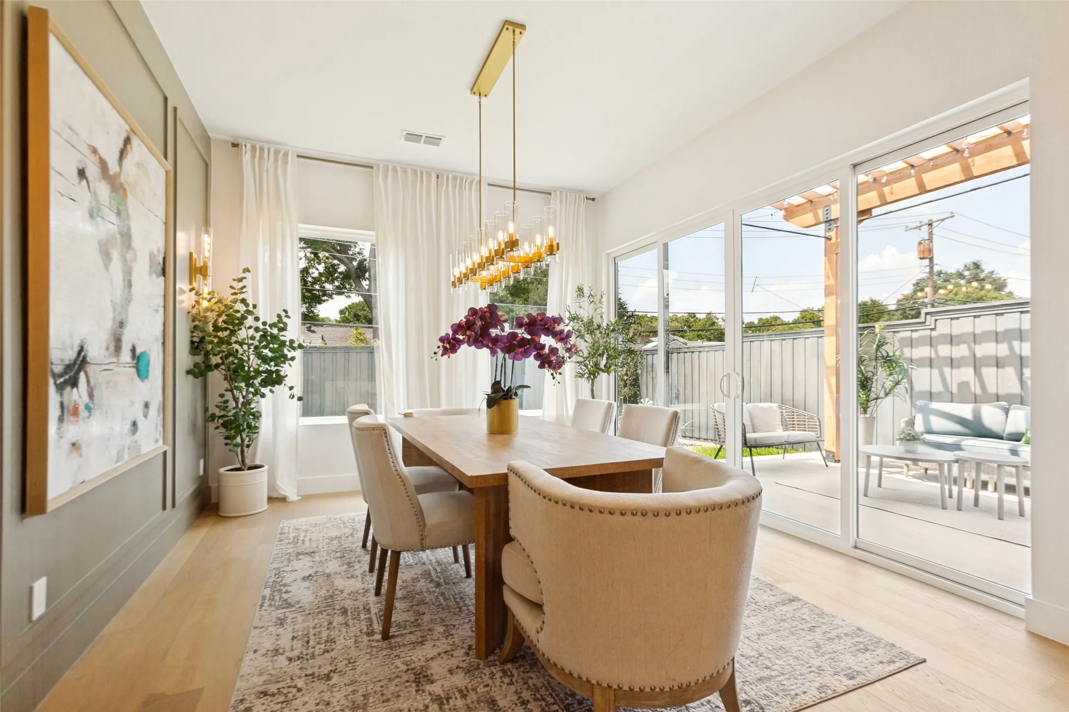 Dining area featuring oak wood flooring, designer light sconces, linear chandelier, and board and batten accent wall.