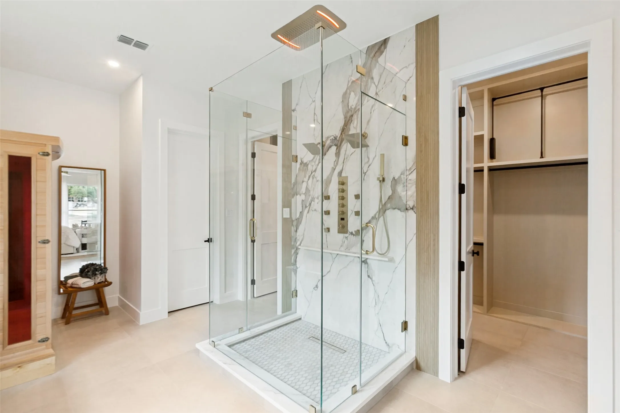 Spacious dual walk-in shower with multiple spray heads, overhead rainshower head, clear glass enclosure and Designer marble-patterned tiles.