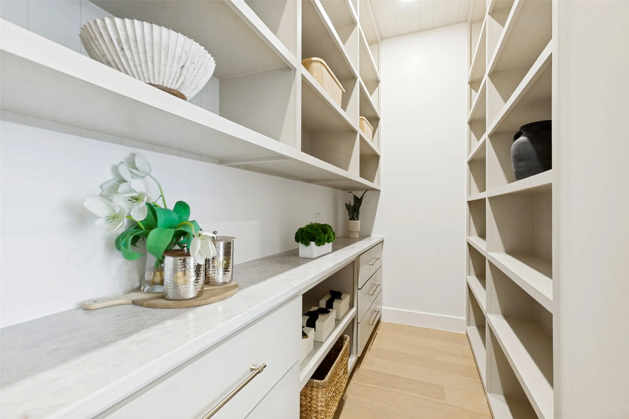 Walk-in custom pantry featuring extensive built-in shelving, Designer hardware pulls,quartz countertop, and oak wood flooring.