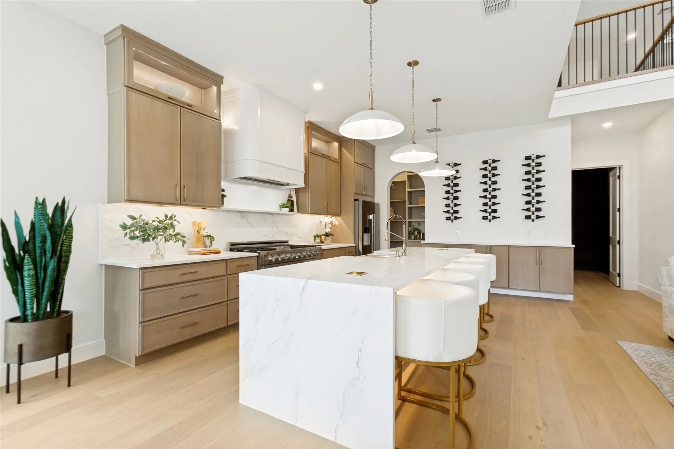 Open-concept kitchen with white oak wood soft close cabinetry, and designer hardware. An oversize quartz waterfall island, designer vented hood, and built-in range.