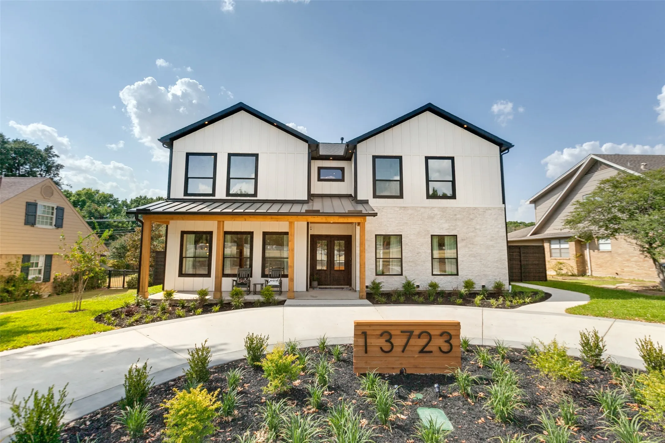 Contemporary two-story Modern Farmhouse featuring white siding, stone and cedar wood trim with a covered front porch supported by cedar wood columns.