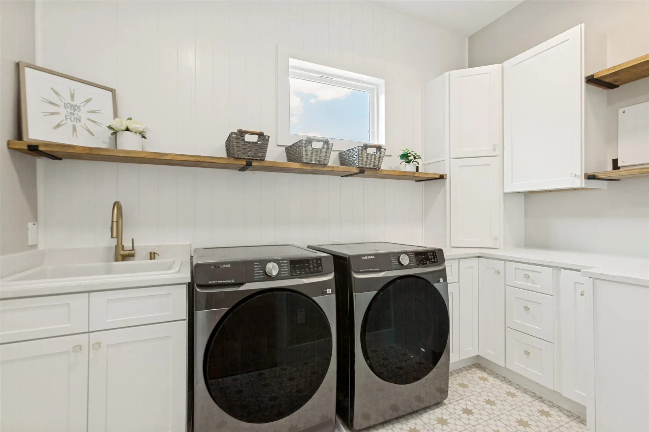 Large laundry room on 2nd floor with white shaker cabinetry, designer cement tile flooring, wood shelving, utility sink, and a window for natural light.
