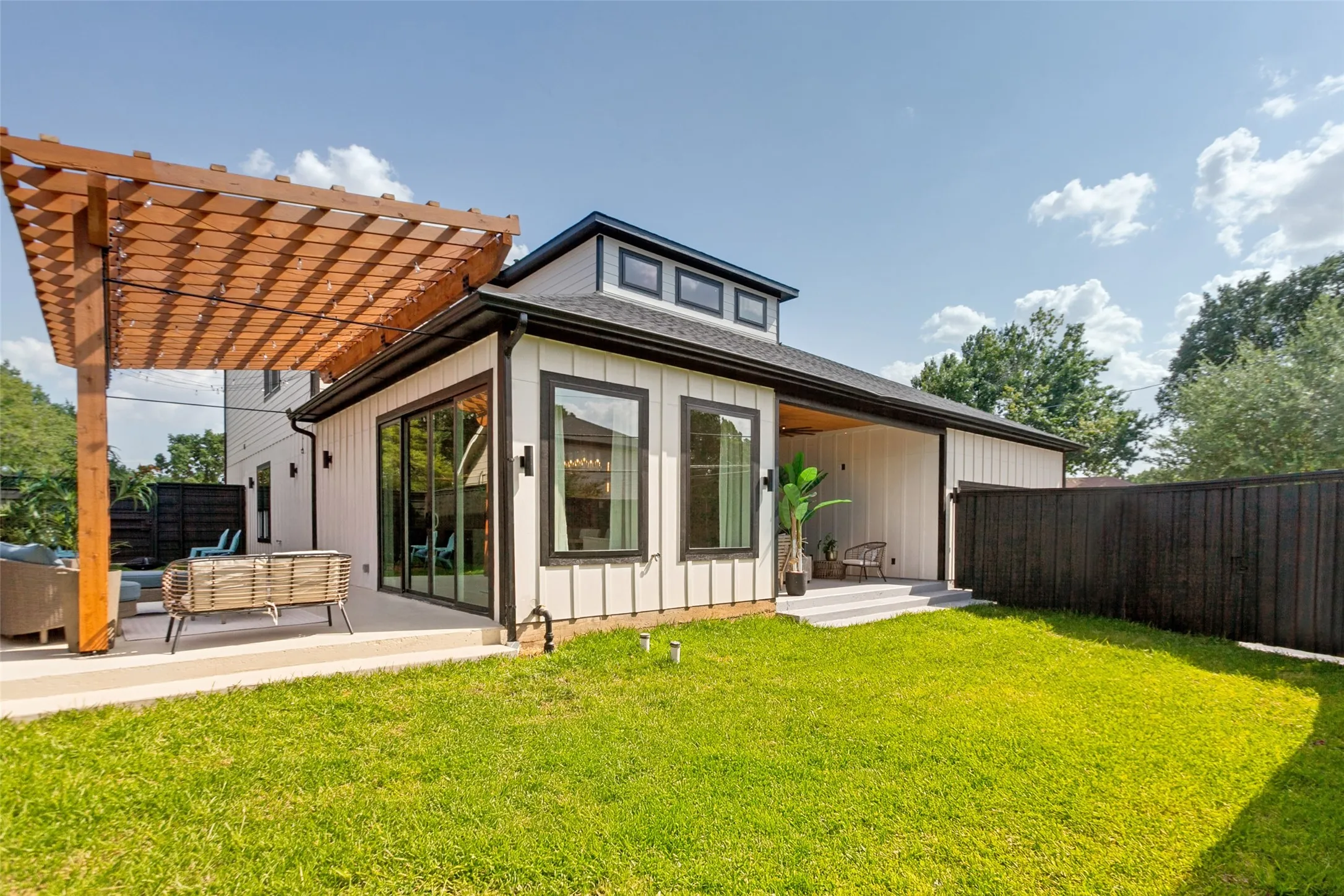 Expansive outdoor area with multiple entertaining areas, one open patio with a wooden pergola, and an additional covered patio with large designer ceiling fan.