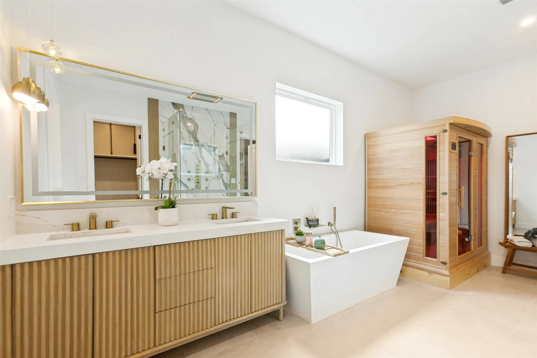 Dual wood vanity with designer light fixtures, an oversized mirror, infrared therapy sauna and a freestanding jetted soaking tub.