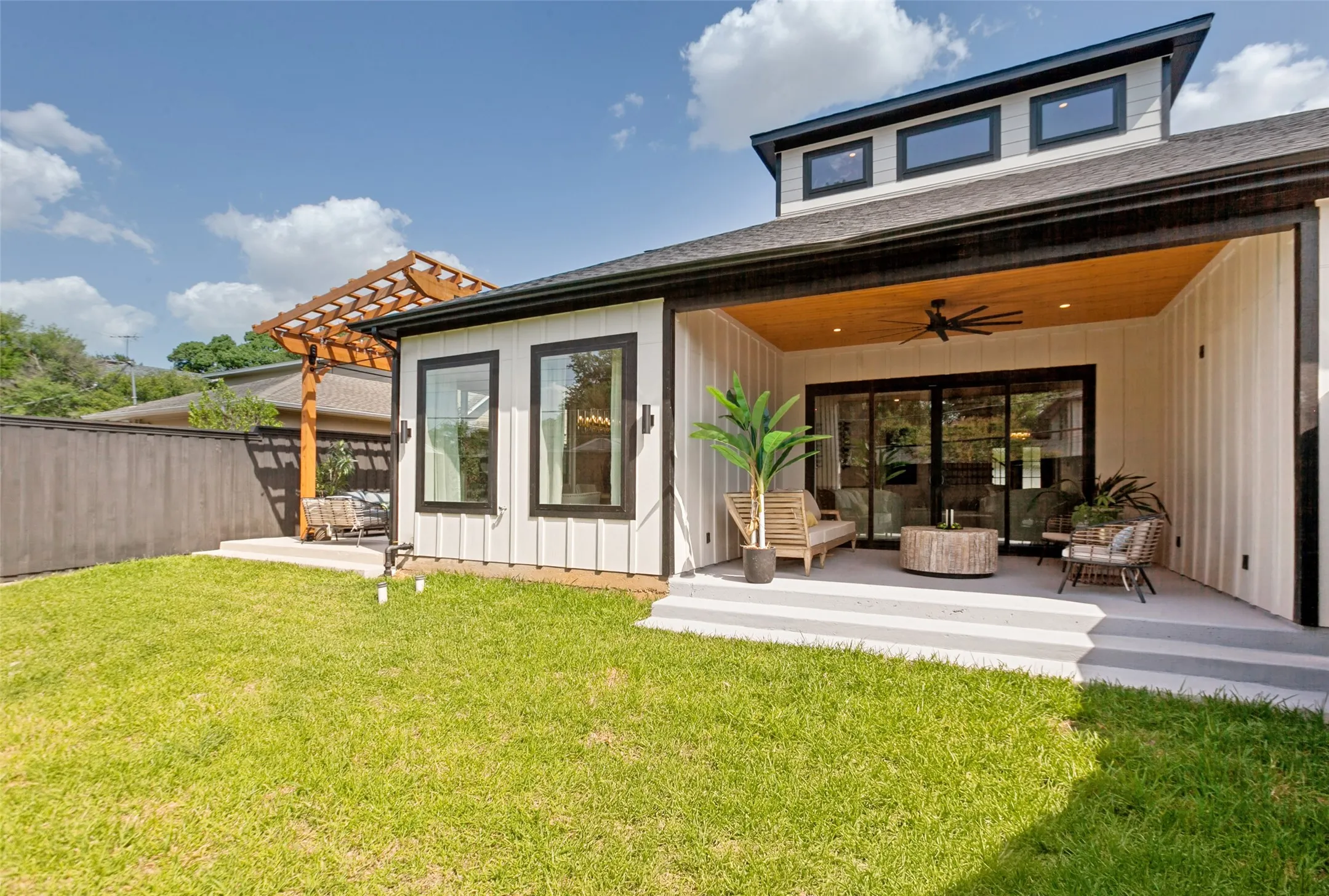 Expansive green lawn with a covered patio featuring a cedar wood ceiling, ceiling fan, and sliding glass doors.