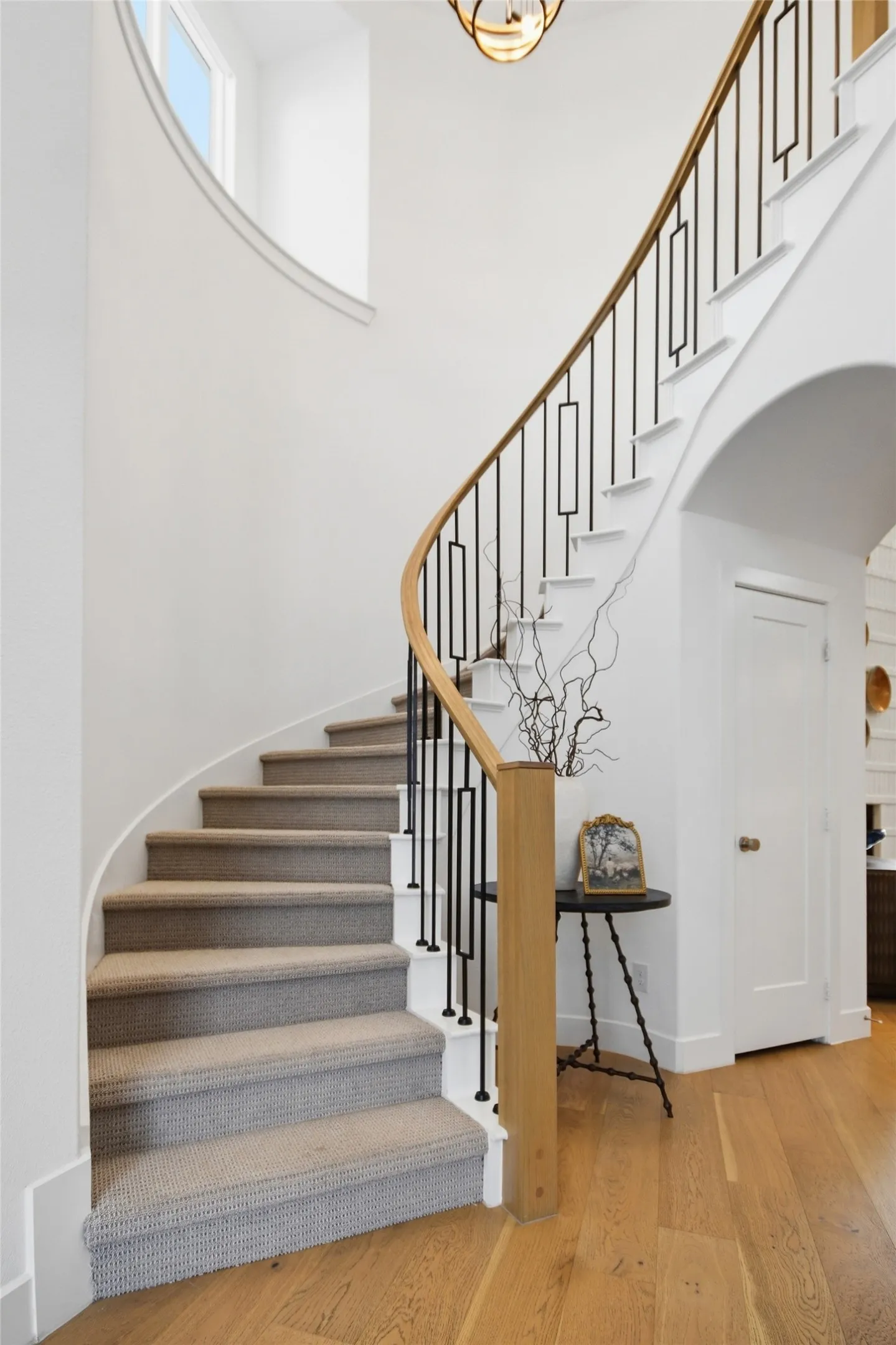 Sweeping curved staircase with light wood flooring, plush stair carpeting, contemporary black metal balusters, and a light wood handrail