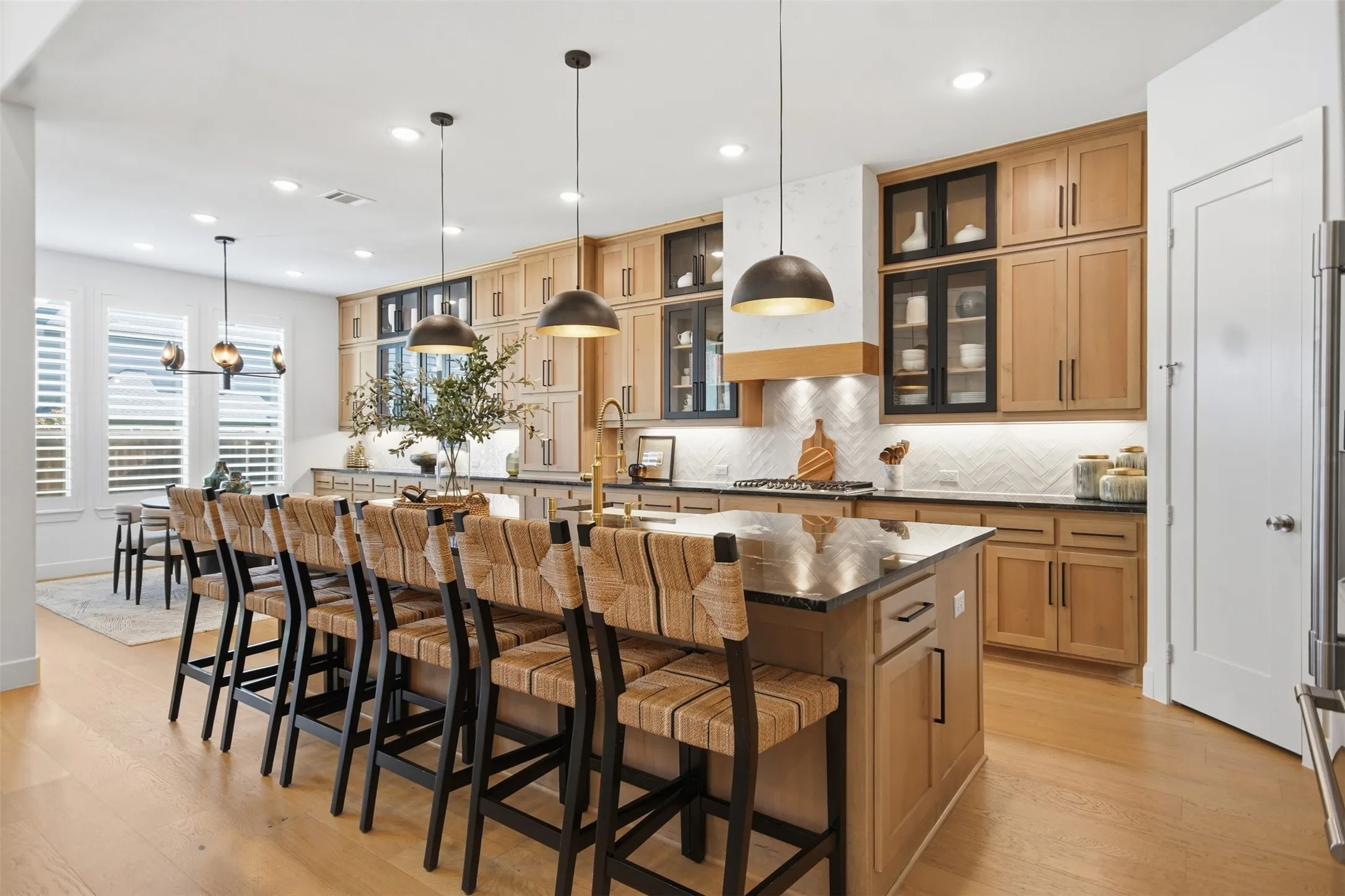 Chef's Dream Kitchen featuring an expansive center island with seating, natural wood cabinetry, a herringbone tile backsplash, integrated range hood, and wood-finish flooring