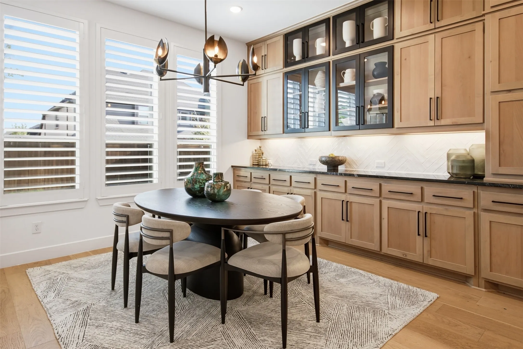 Dining area featuring a contemporary chandelier, three tall windows with white plantation shutters, and light wood-finish flooring