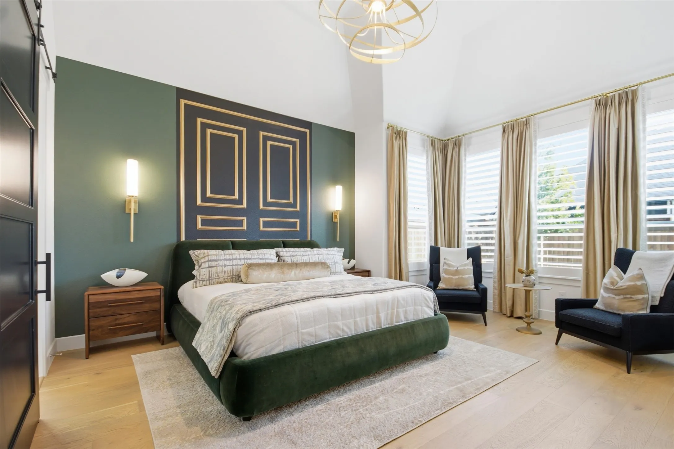 Vaulted ceiling bedroom featuring a decorative accent wall with gold-finished trim, built-in wall sconces, wood-finish flooring, and multiple windows with plantation shutters